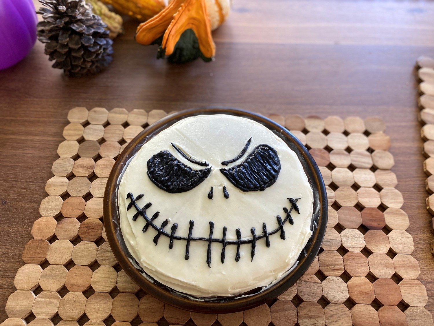 A single round cake frosted white, with Jack Skellington’s eyes, nose and stitched smile drawn in black decorating gel.