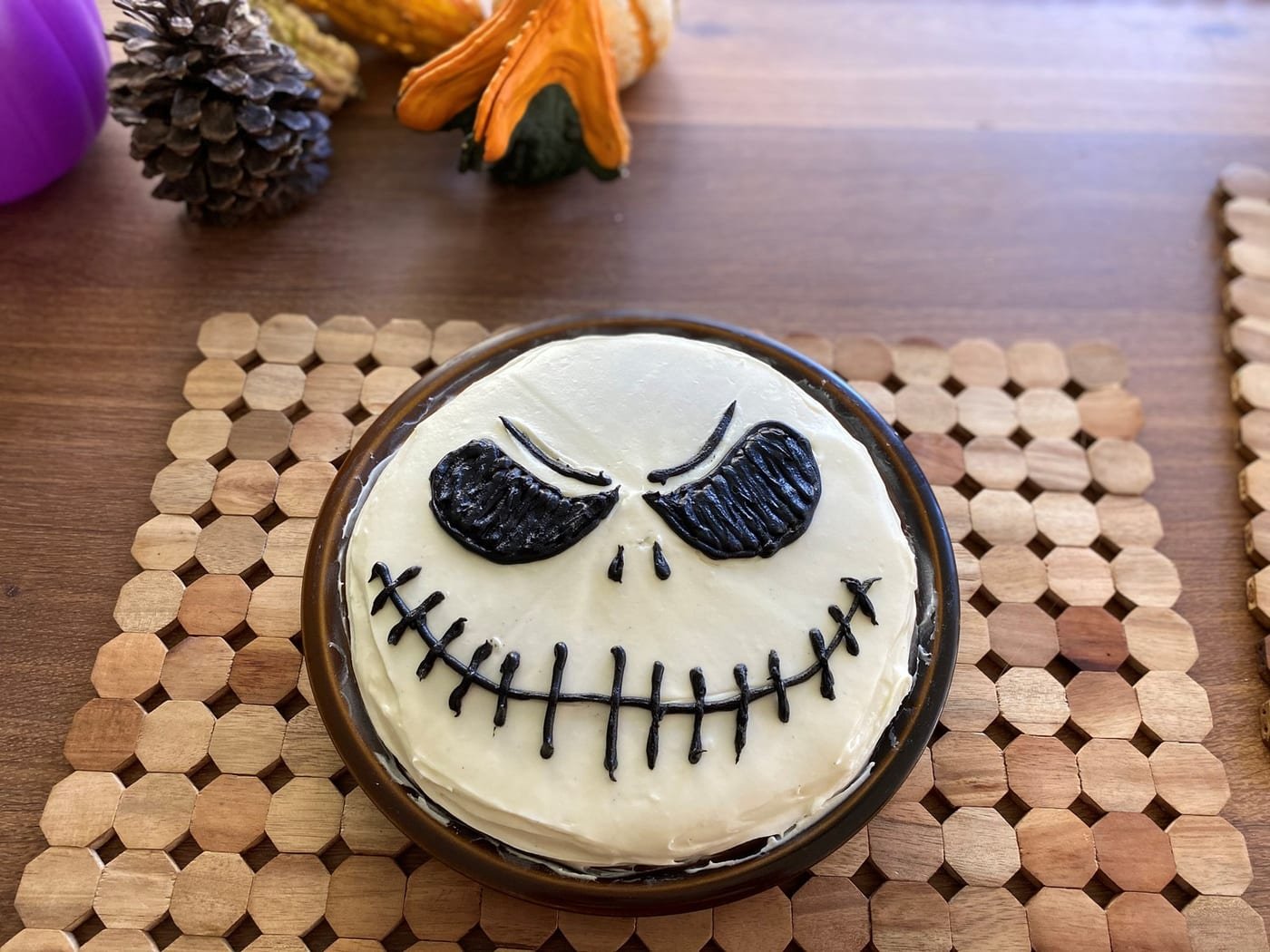 A single round cake frosted white, with Jack Skellington’s eyes, nose and stitched smile drawn in black decorating gel.