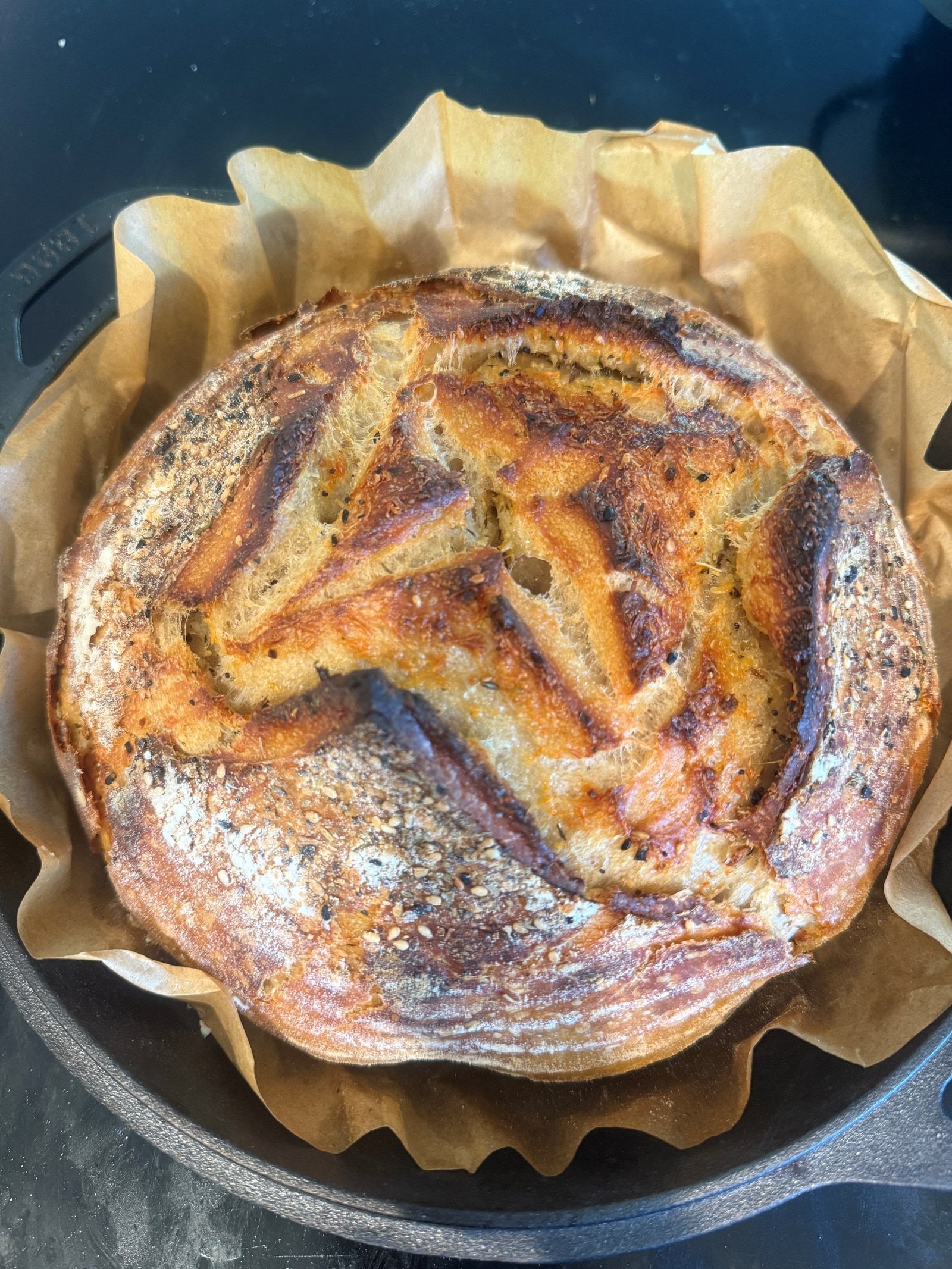 Sourdough loaf with a golden crust in a cast-iron baker lined with parchment