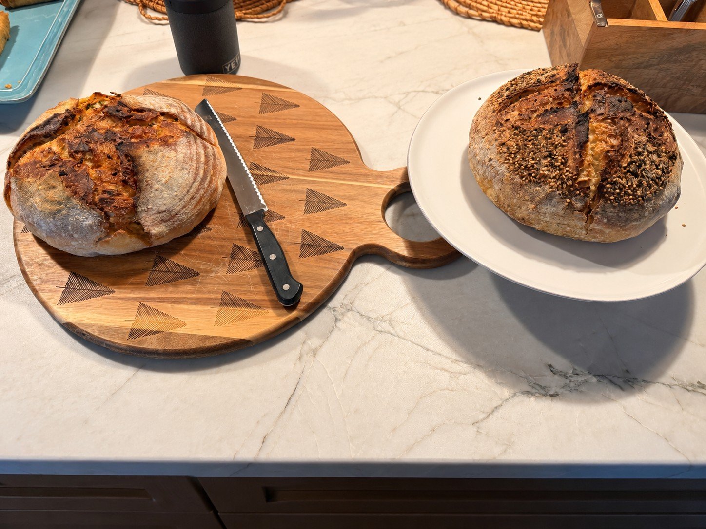 Two homemade sourdough loaves, one on a wooden cutting board and one on a white plate